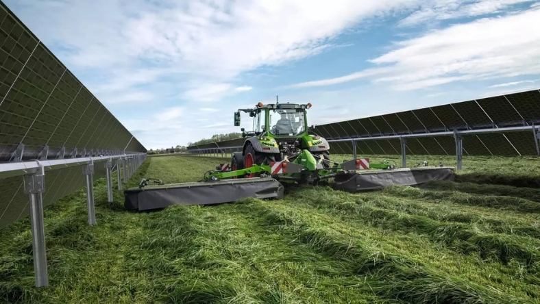 Agricultural machinery operating in a field alongside solar panels